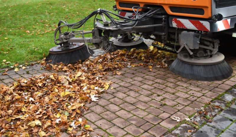 Sweeper sweeps leaves in autumn