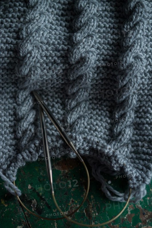 Grey knitted piece with knitting pattern and knitting needles