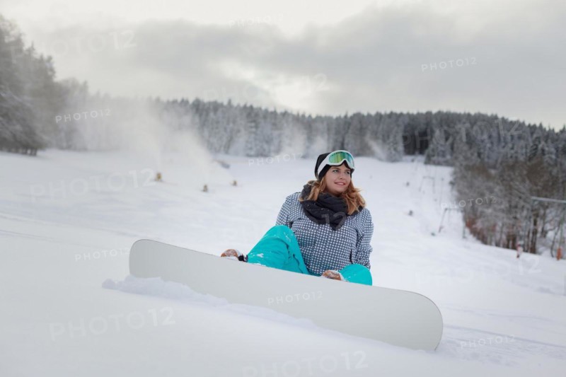 Woman with snowboard sitting in the snow