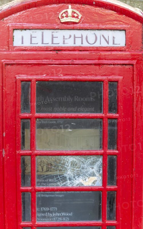 Smashed vandalised glass panel of old red telephone box