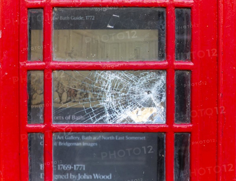 Smashed vandalised glass panel of old red telephone box
