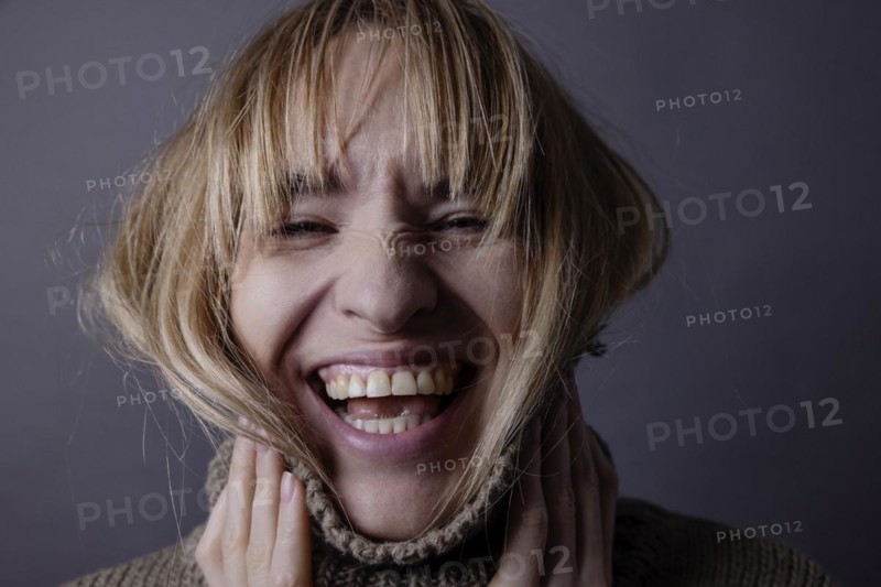 Young woman with turtleneck jumper and long hair laughs into camera
