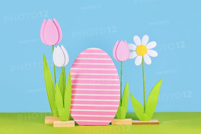Easter arrangement with felt spring flowers and wooden easter egg in front of blue background