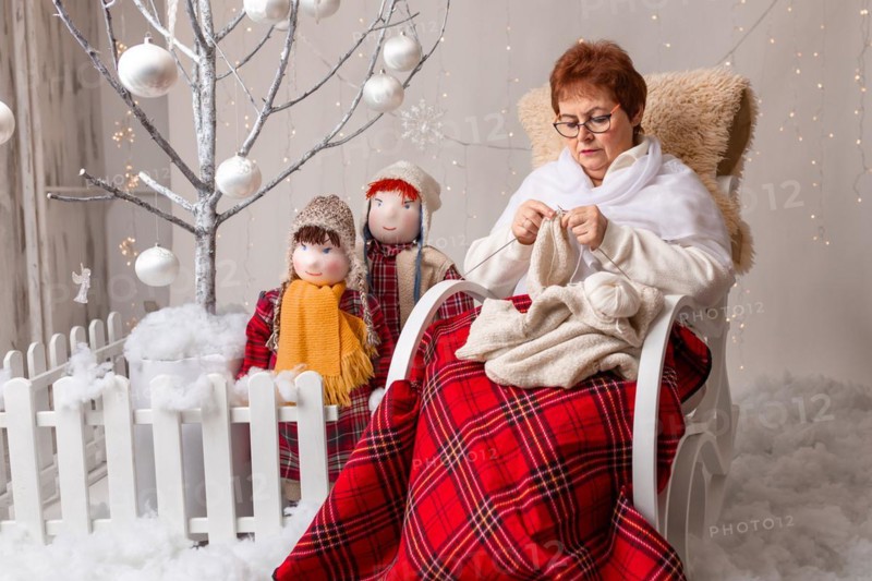 A nice elderly woman sews to knit her granddaughters in a Christmas arrangement. In studio