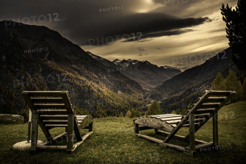 Deck chairs on a mountain meadow with autumnal mountain forest and threatening cloudy sky