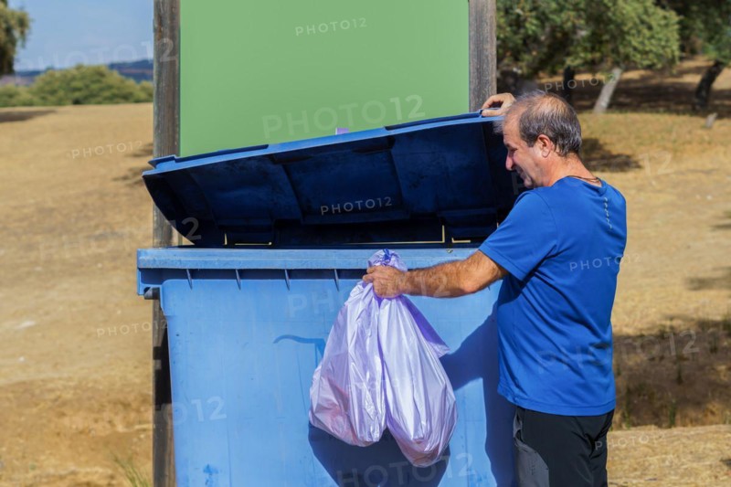 Man throwing garbage bags into a dumpster with a blank sign for copy space