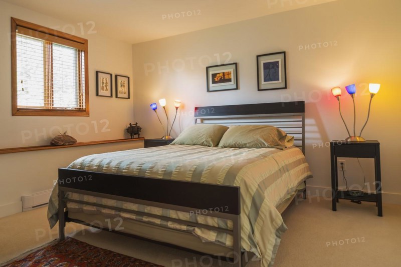 Black wood and gray metal frame queen size bed with striped beige bedspread in guest bedroom inside modern home