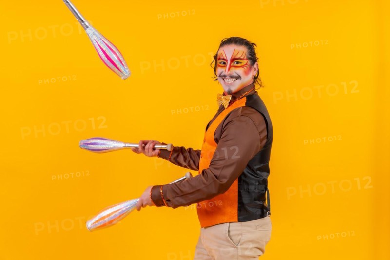 Juggler in a vest with makeup juggling with maces on a yellow background