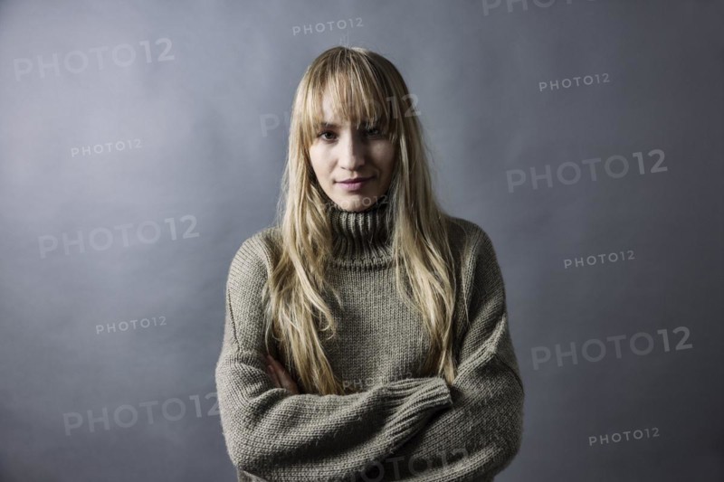Woman with long blond hair and warm woollen jumper crosses her arms