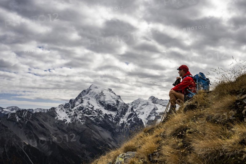 Mountaineer on autumnal mountain meadow with cloudy sky in front of Ortler summit massif