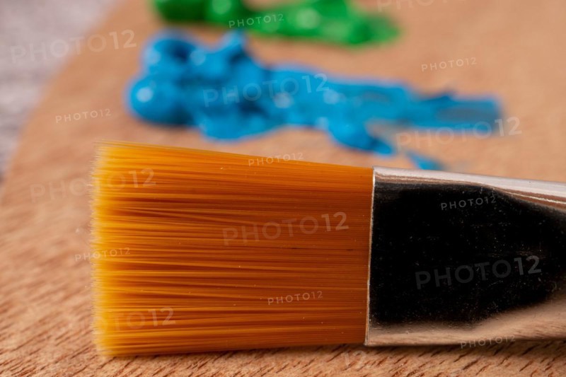 Close-up brush with out-of-focus oil paint colors on a wooden palette
