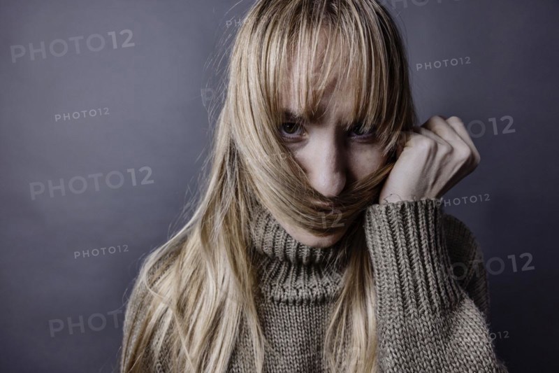 Young woman with long blond hair coquettishly holding a strand of hair in front of her mouth