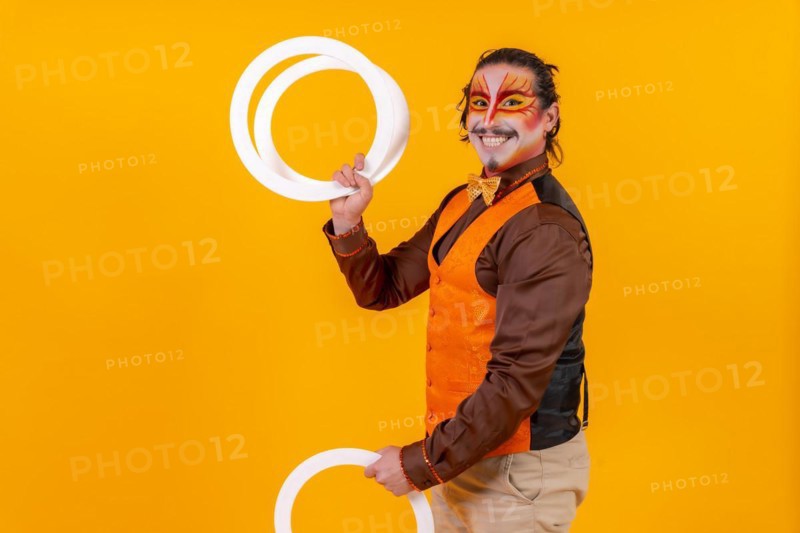 Juggler in a vest and with a painted face juggling hoops on a yellow background