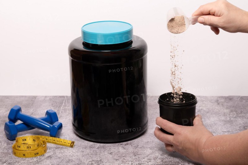 Woman pouring a scoop of protein powder in an insulated shaker on a black background