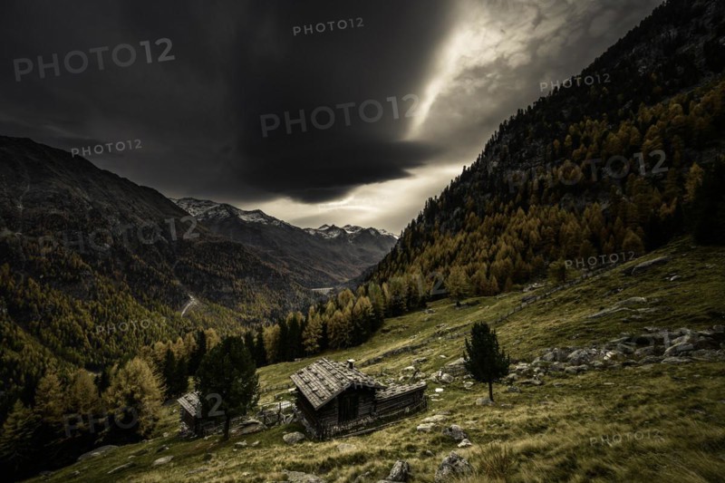 Mountain hut on mountain meadow with autumnal mountain forest and threatening cloudy sky