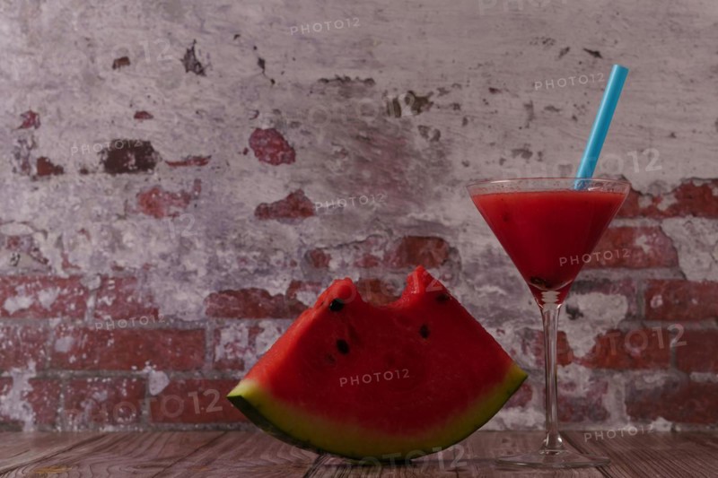 Cocktail glass with watermelon juice and slices of fresh watermelon on a wooden table