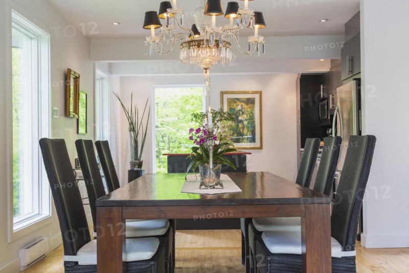 Walnut colored wooden dining table with black high back wicker chairs in dining room inside modern home