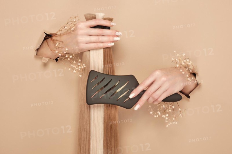 Hands with flowers hold strands of hair for extensions on a beige background. hair beauty