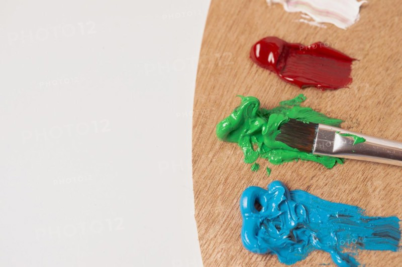 Wooden palette with colored oil paints and brushes isolated on a white background