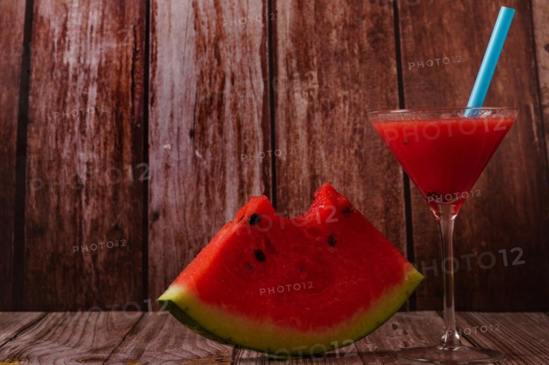 Cocktail glass with watermelon juice and slices of fresh watermelon on a wooden table