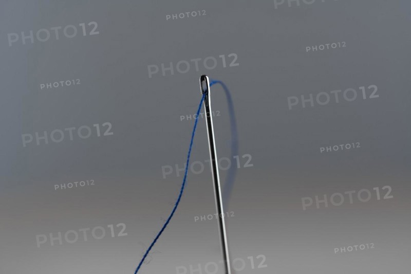 Sewing needle and blue thread against a neutral background