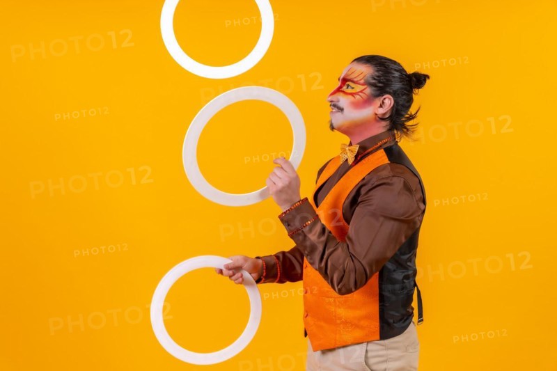 Juggler in a vest and with a painted face juggling hoops on a yellow background