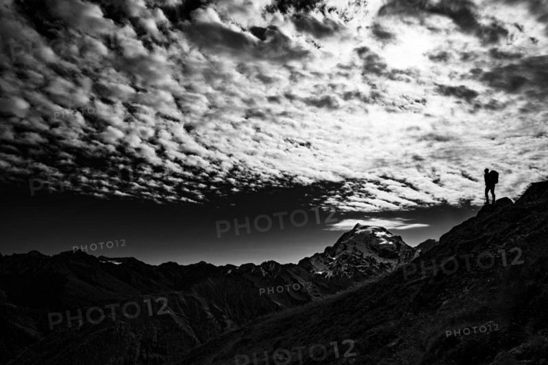 Mountaineer in backlight with cloudy sky in front of Ortler summit massif