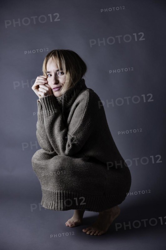 Squatting young woman with long blond hair has pulled knitted jumper over her knees