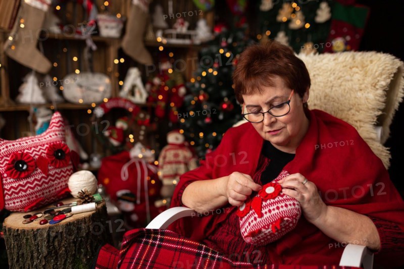 Grandmother sews a plush owl in Christmas arrangement. In studio