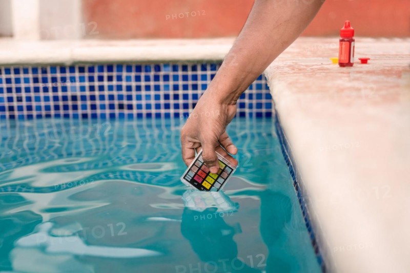 Close up of person testing the ph of the water with mini tester in swimming pool. Hand testing pool water for chlorine with PH mini tester. Testing the chlorine and PH of swimming pool