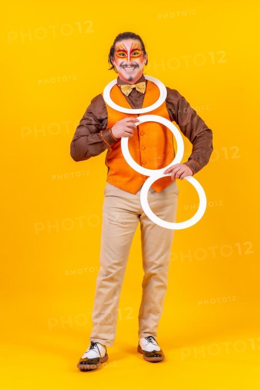 Happy juggler man in makeup vest juggling hoops on a yellow background