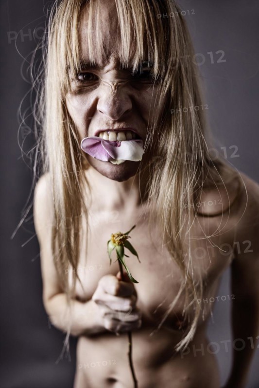 Young naked woman eating the petals of a rose and looking aggressively into the camera