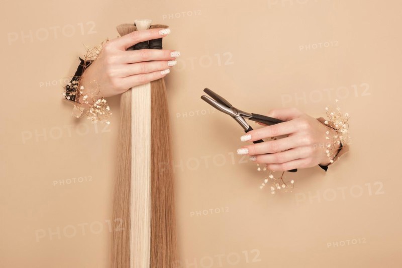 Hands with flowers hold strands of hair for extensions on a beige background. hair beauty
