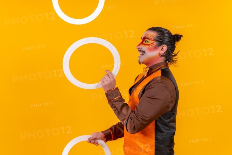 Portrait of a juggler in a vest with a painted face juggling hoops on a yellow background
