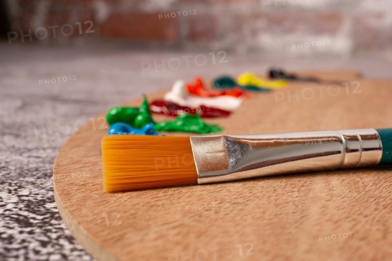 Close-up brush with out-of-focus oil paint colors on a wooden palette