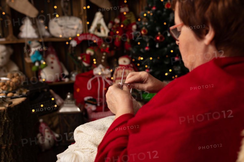Grandmother sews a plush owl in Christmas arrangement. In studio