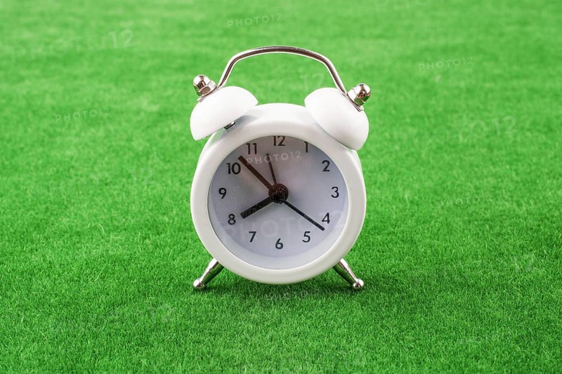 White color alarm clock a on a green grass background