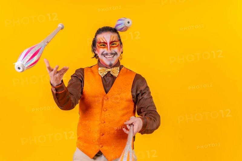 Juggler in a vest with makeup juggling with maces on a yellow background