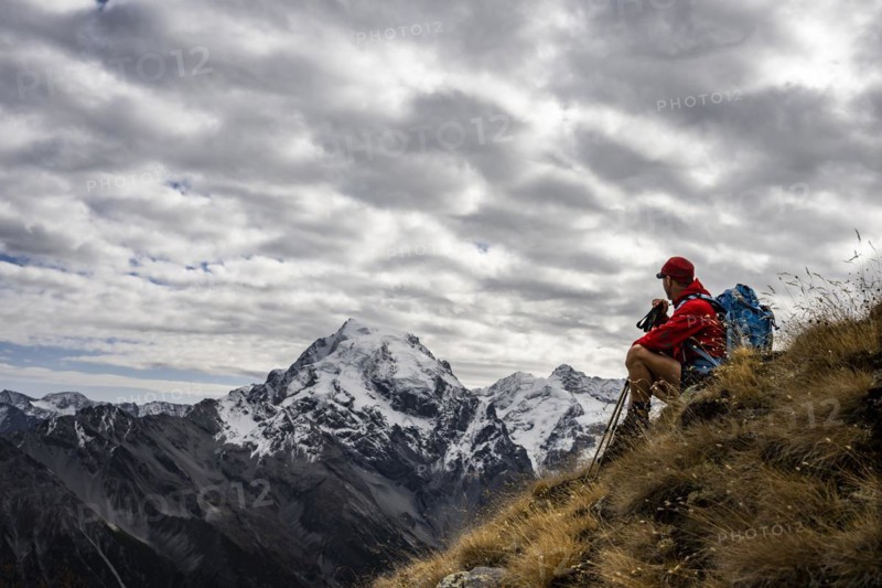 Mountaineer on autumnal mountain meadow with cloudy sky in front of Ortler summit massif