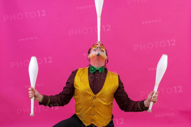 Clown with white facial makeup on a pink background