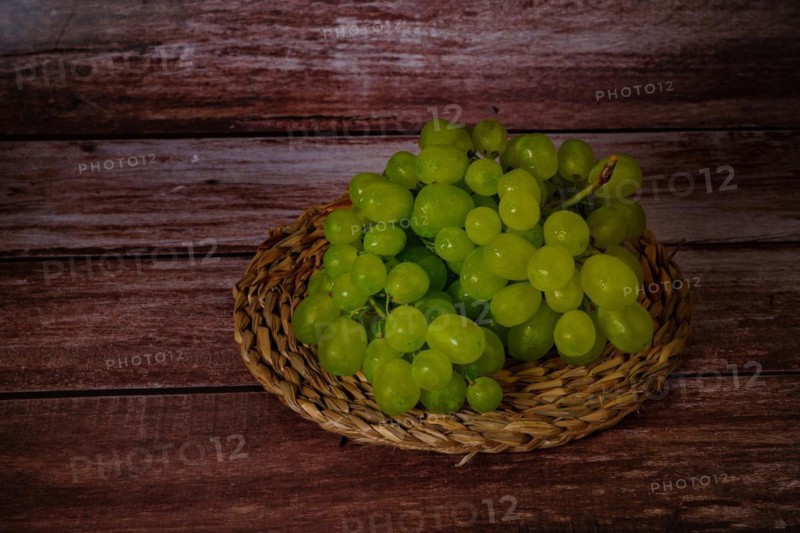 Close-up of a bunch of green grapes on an esparto grass tray with a dark wood background