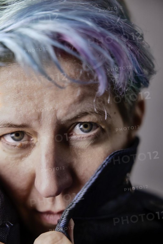 Androgynous woman with dyed hair pulls up the collar of her denim jacket