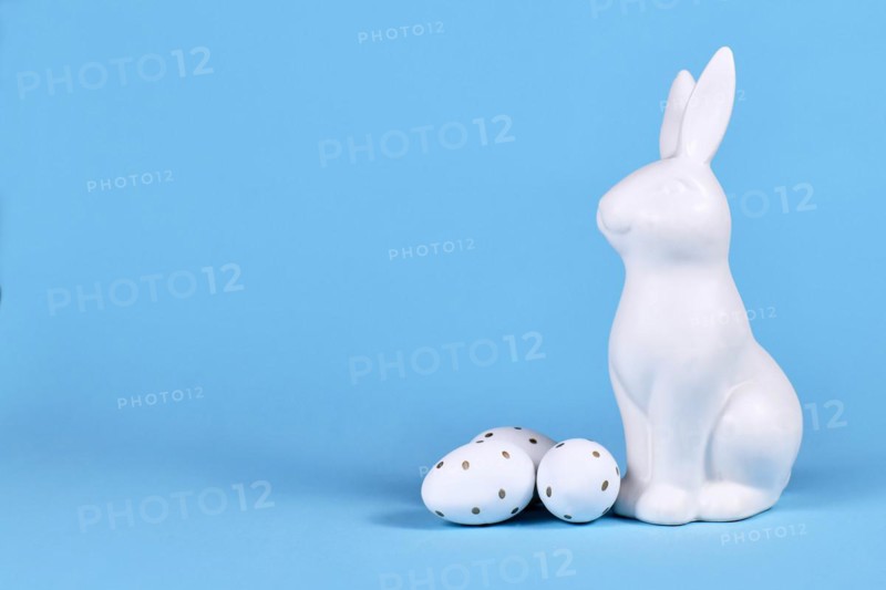 Easter bunny and white and gold Easter eggs with dots on blue background with copy space