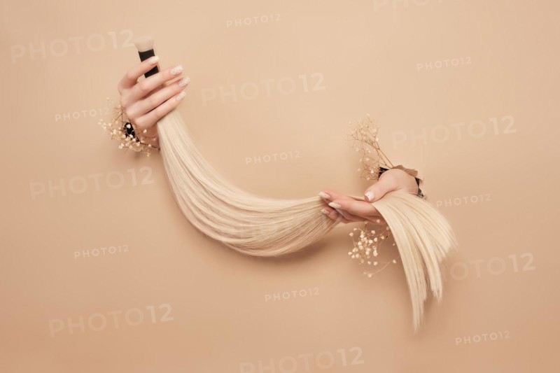 Hands with flowers hold strands of hair for extensions on a beige background. hair beauty