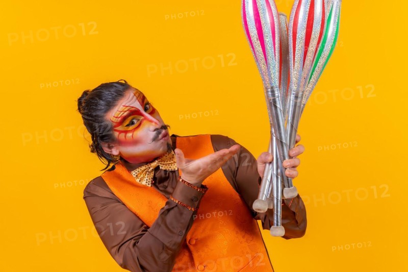 Kiss and portrait of happy juggler man in makeup vest juggling clubs on yellow background