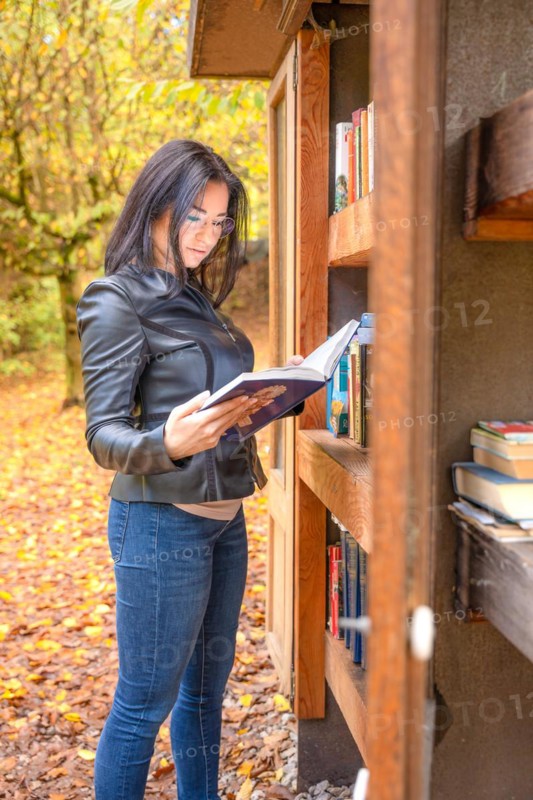 Attractive woman looking into books next to bookshelf in forest
