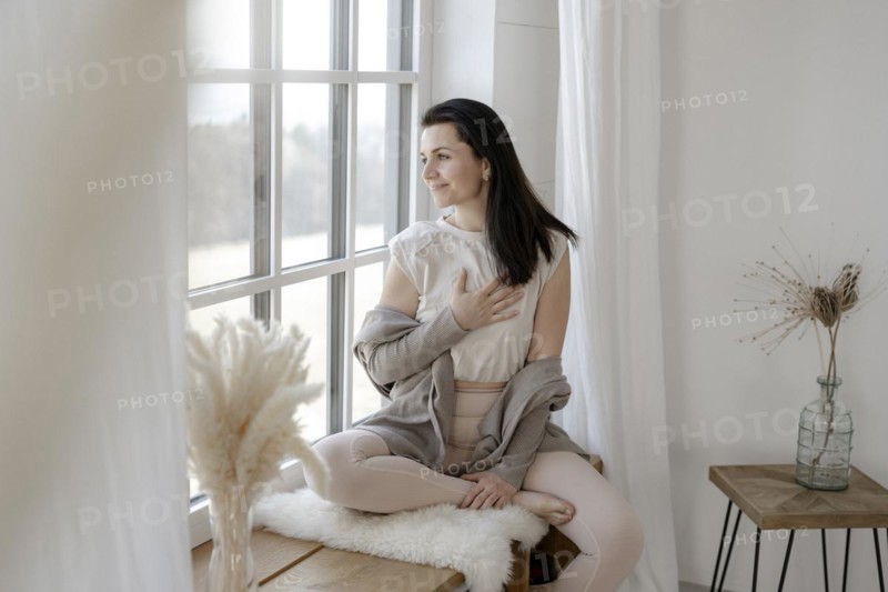 Satisfied woman sits gratefully by the window