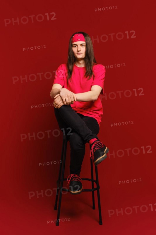 Young man sits on high chair with his leg on his leg