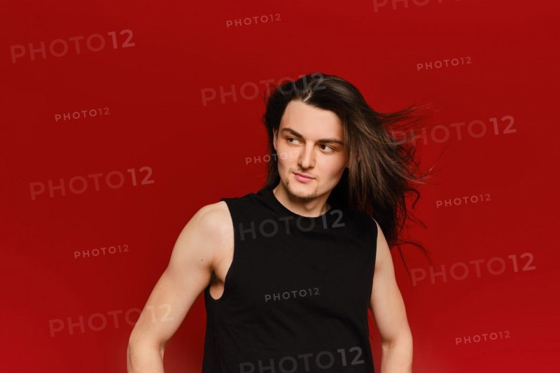 Studio portrait of young handsome man with waiving long hair on red background