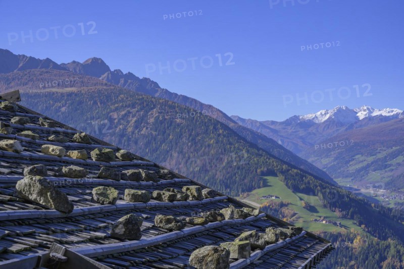 Shingle roof weighted down with stones behind it snow-covered mountains above the Ulten Valley seen from the Pfrollnhof wine tavern